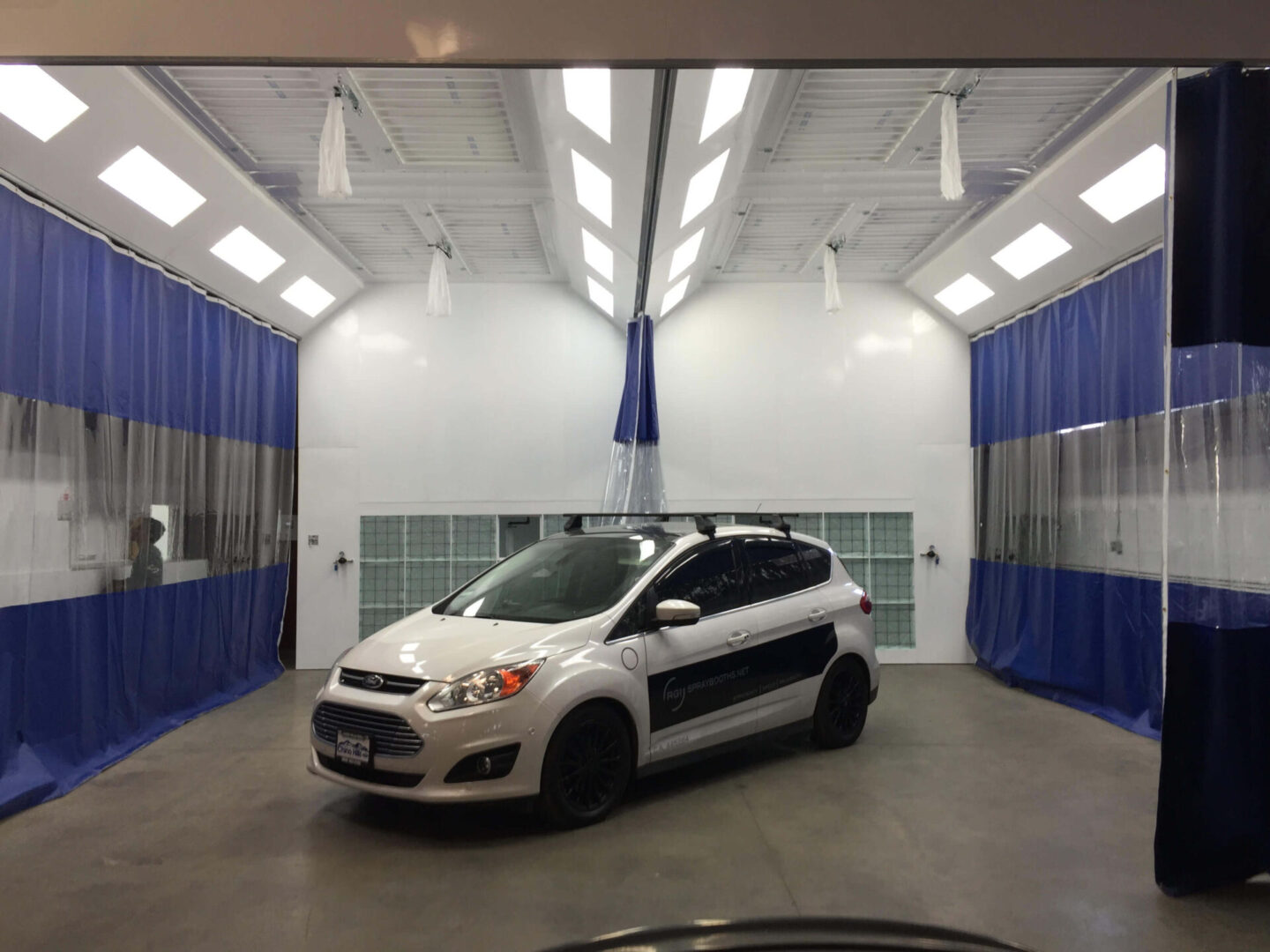 A white subaru impreza station wagon with company logos parked in a brightly lit vehicle inspection bay with blue curtains.