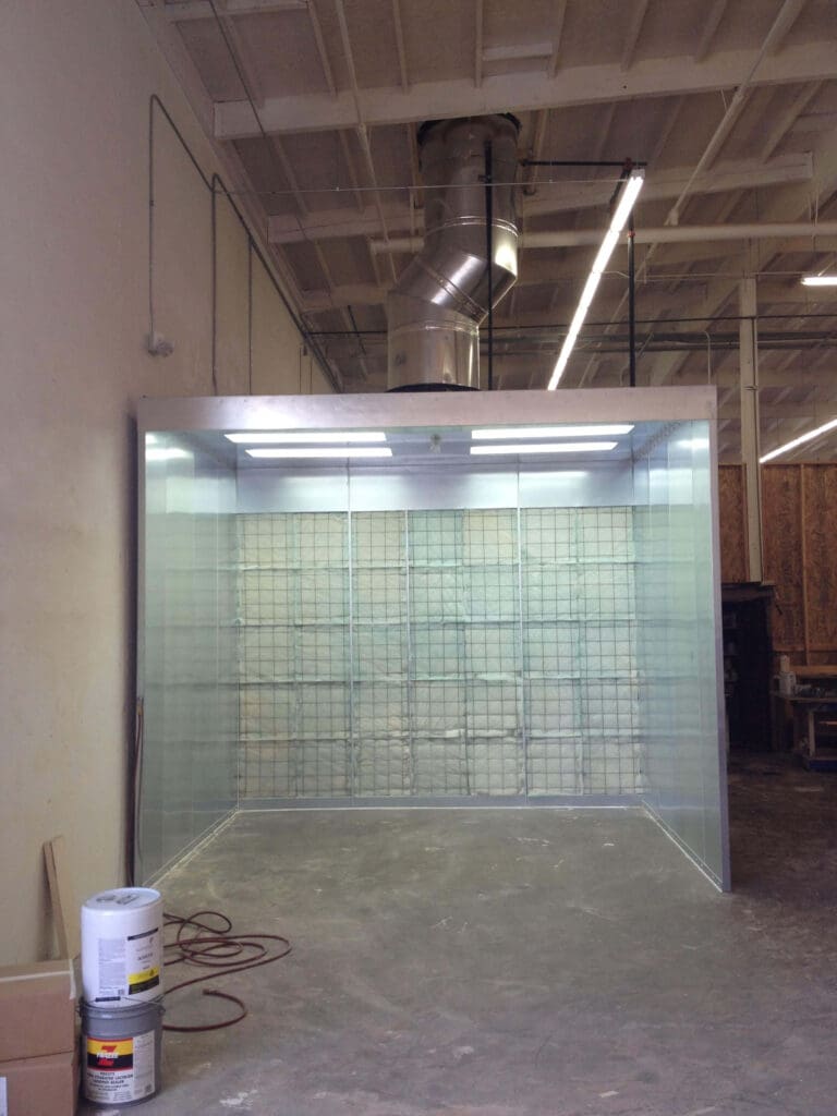 A transparent enclosure with a wire mesh screen filled with sandbags inside an industrial workshop.