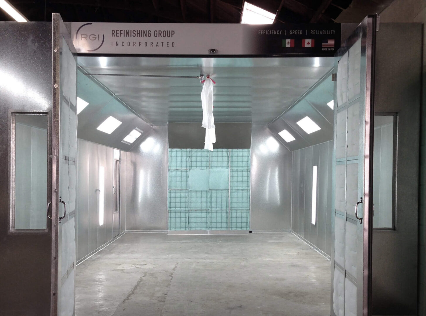 A large industrial paint booth with open doors, featuring a white car hood suspended in the center, and the company's name "refinishing group incorporated" displayed above.