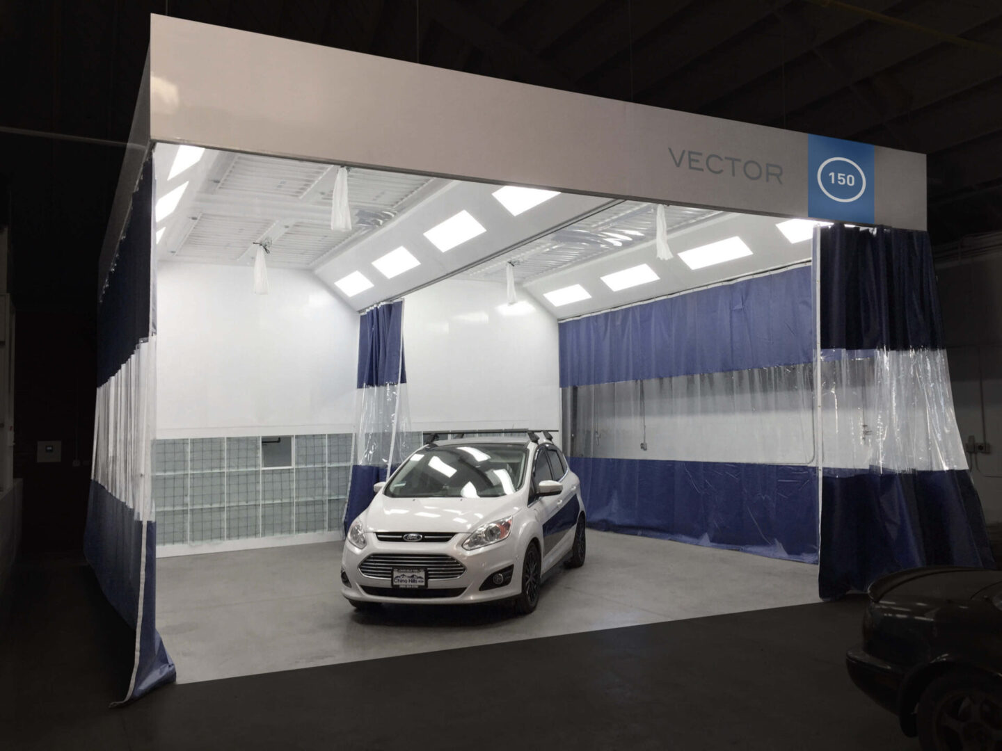 A white car displayed inside a spacious booth with blue curtains and the label "vector 150" at a trade show.