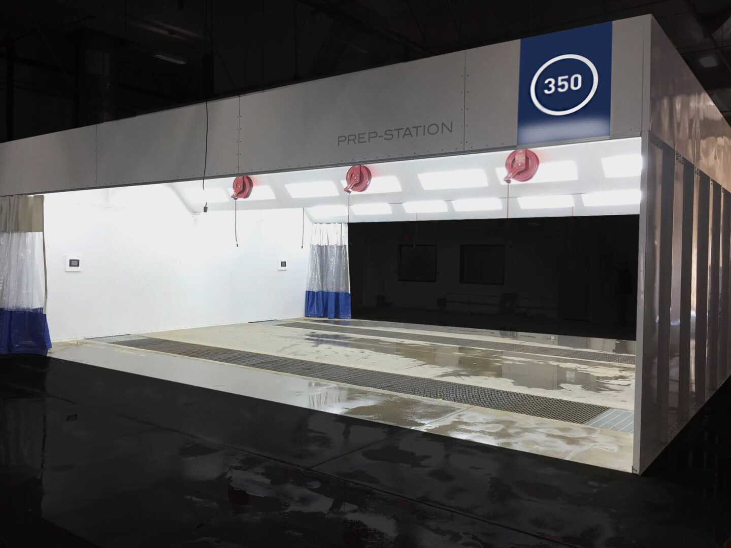 A large, empty automotive prep station with reflective floor, blue and white branding, and overhead lighting in an industrial building.