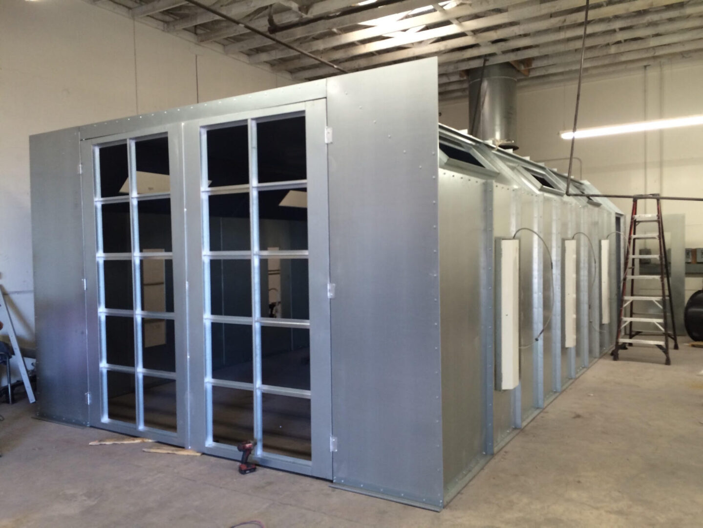 Large industrial air duct system under construction in a warehouse, featuring a metal framework and glass windows.