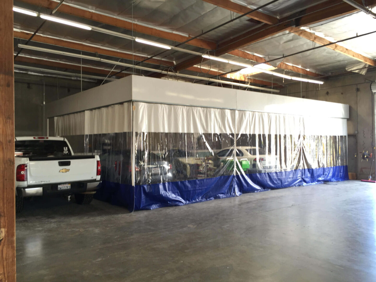 A large temporary enclosure with transparent walls and blue skirts inside a warehouse, with a pickup truck parked beside it.