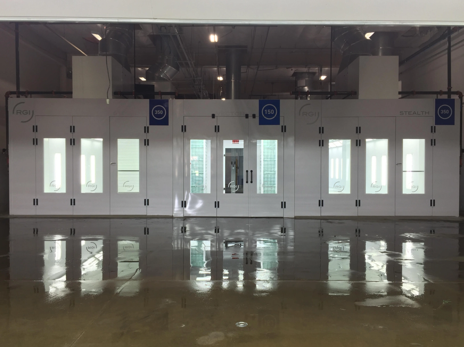 Glossy floor reflecting a row of closed garage doors with logos and numbers, in a spacious industrial building.