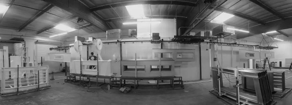 Black and white image of a spacious industrial workshop with various machinery and storage racks.