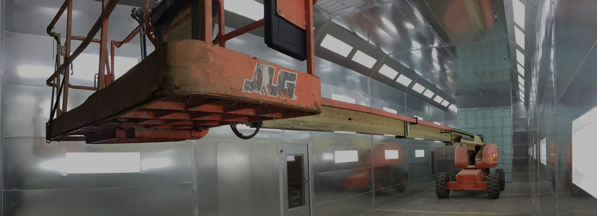 An orange telescopic boom lift parked inside an industrial building with metal walls and large doors.